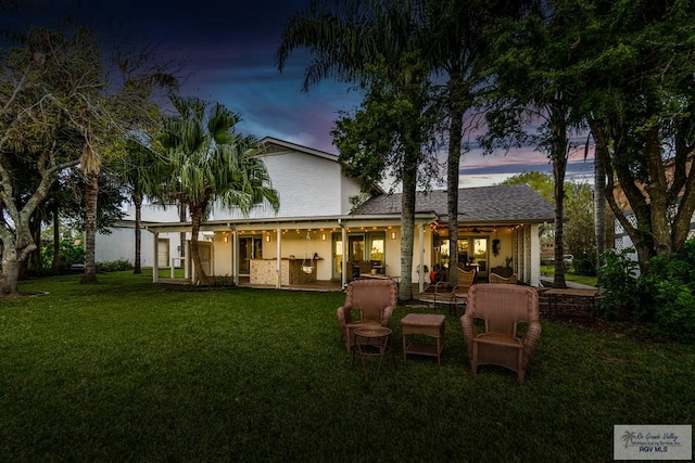 back house at dusk with a patio area and a yard