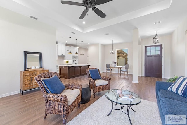 living area with light wood-type flooring, visible vents, a tray ceiling, recessed lighting, and baseboards