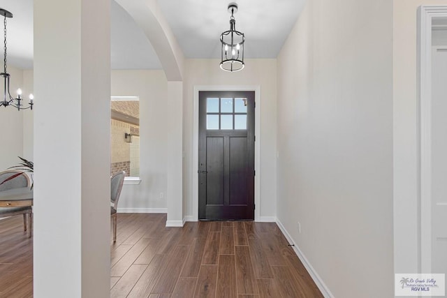 foyer entrance with dark wood-type flooring, a notable chandelier, arched walkways, and baseboards