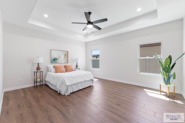 bedroom with recessed lighting, a tray ceiling, baseboards, and wood finished floors