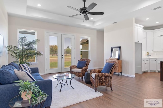 living area featuring visible vents, light wood-style flooring, recessed lighting, french doors, and a raised ceiling