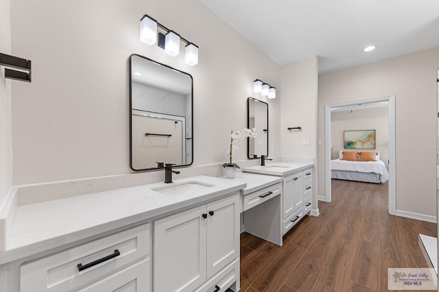 ensuite bathroom with a sink, recessed lighting, wood finished floors, and double vanity