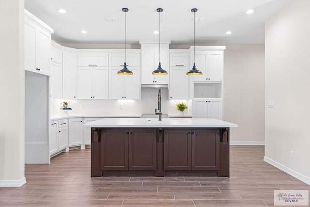 kitchen with a kitchen island with sink, white cabinets, a sink, and light wood finished floors