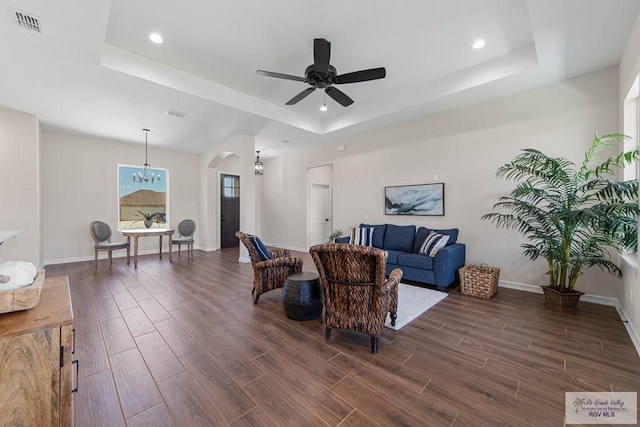 living room with a ceiling fan, visible vents, dark wood finished floors, a tray ceiling, and arched walkways