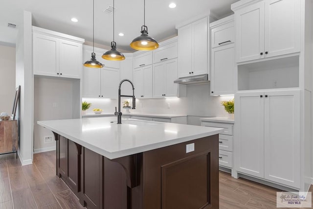 kitchen featuring under cabinet range hood, visible vents, a center island with sink, and white cabinets