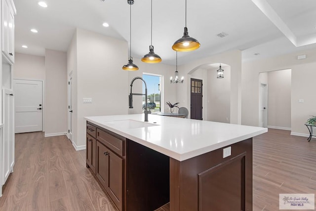 kitchen featuring arched walkways, visible vents, light wood-type flooring, and a sink