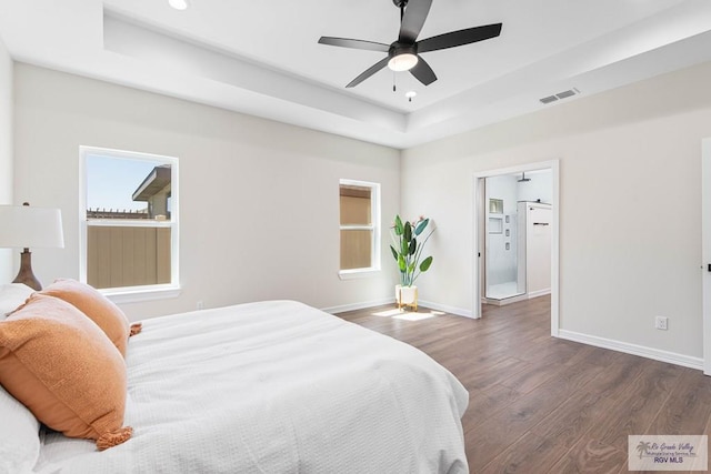 bedroom featuring visible vents, baseboards, a tray ceiling, and wood finished floors