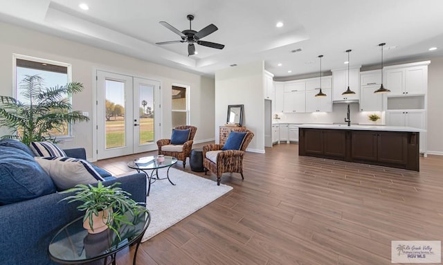 living room featuring recessed lighting, french doors, a raised ceiling, and wood finished floors