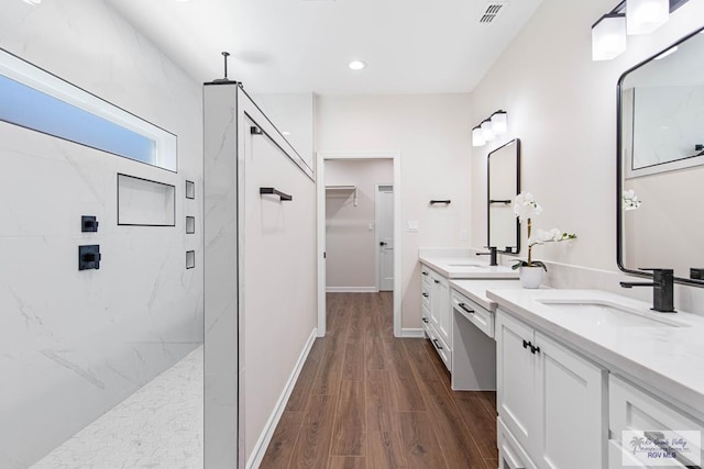 full bath featuring wood finished floors, visible vents, a marble finish shower, double vanity, and a sink