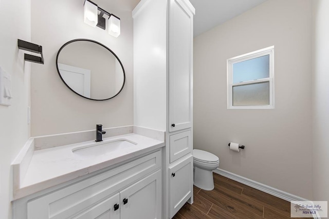 bathroom with vanity, toilet, wood finished floors, and baseboards