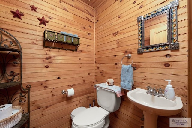 bathroom with wood walls, sink, and toilet