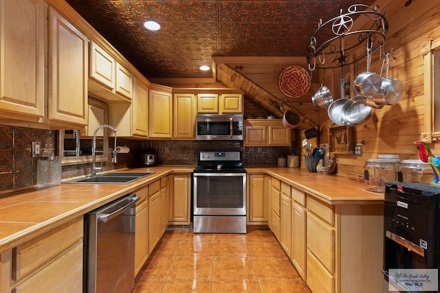 kitchen with light brown cabinets, stainless steel appliances, wooden walls, and sink