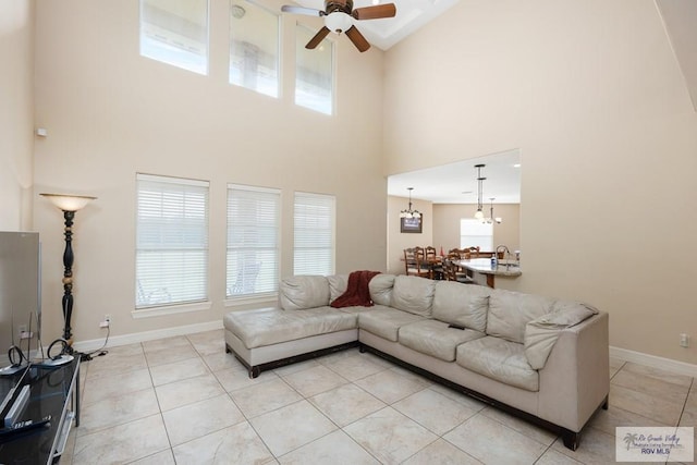 tiled living room featuring ceiling fan with notable chandelier and a high ceiling