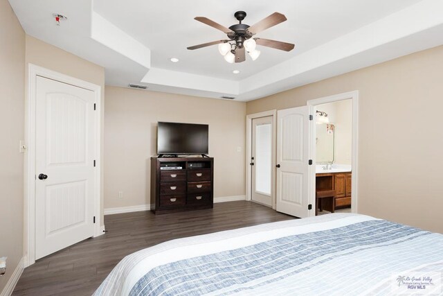 bedroom featuring dark hardwood / wood-style flooring, ensuite bathroom, ceiling fan, and a tray ceiling