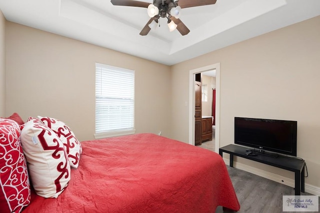 bedroom with wood-type flooring, ensuite bath, a raised ceiling, and ceiling fan