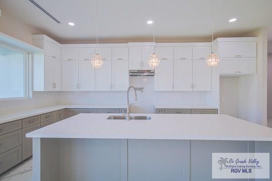 kitchen with a center island with sink, sink, white cabinets, and hanging light fixtures