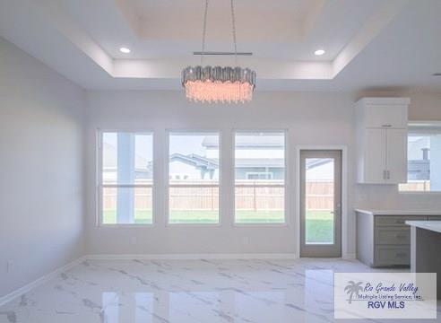 unfurnished dining area featuring a notable chandelier and a raised ceiling