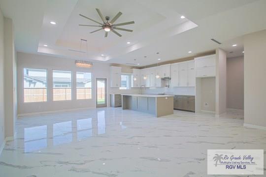 kitchen featuring white cabinetry, sink, ceiling fan, a raised ceiling, and a spacious island