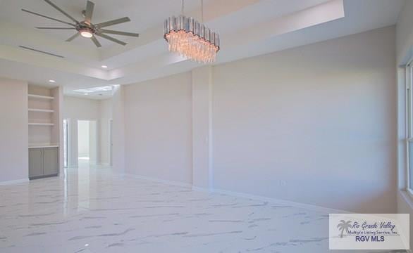 empty room with ceiling fan with notable chandelier and a tray ceiling