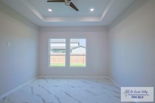 empty room with ceiling fan and a tray ceiling