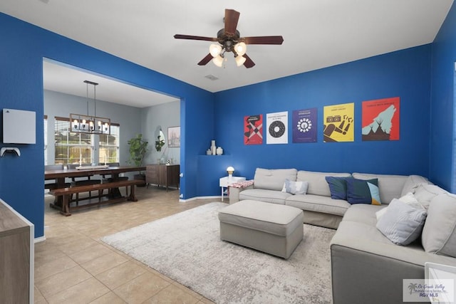 living area featuring tile patterned flooring, visible vents, ceiling fan with notable chandelier, and baseboards