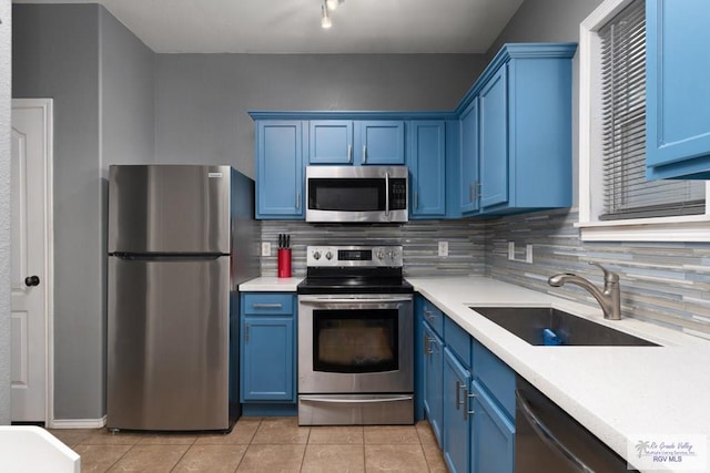 kitchen with backsplash, light tile patterned flooring, stainless steel appliances, blue cabinets, and a sink