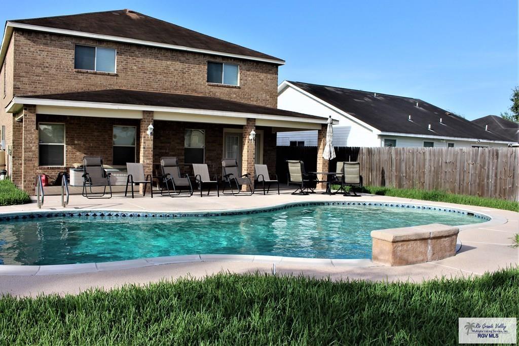 rear view of property with brick siding, a patio area, fence, and a fenced in pool