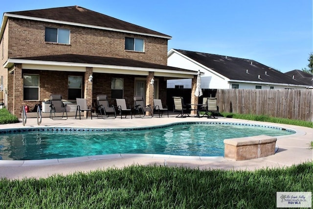 rear view of property with brick siding, a patio area, fence, and a fenced in pool