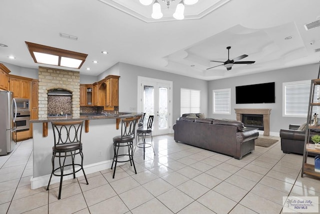 kitchen featuring light tile patterned floors, a raised ceiling, appliances with stainless steel finishes, a peninsula, and a fireplace