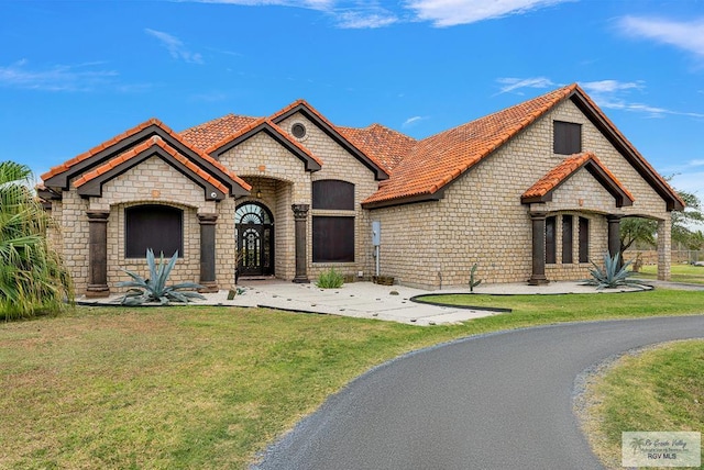 french provincial home with a tiled roof and a front yard