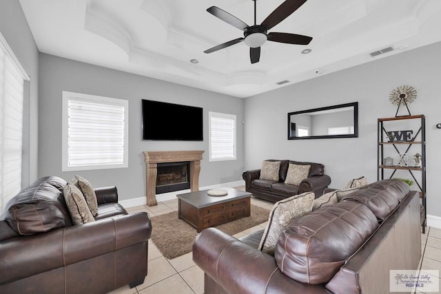 living room featuring light tile patterned floors, a premium fireplace, visible vents, baseboards, and a tray ceiling