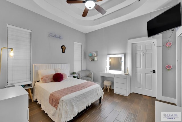 bedroom featuring a tray ceiling, dark wood-type flooring, a ceiling fan, and baseboards