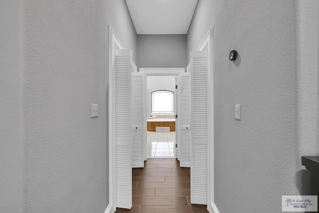 hall with a textured wall, wood finish floors, and baseboards