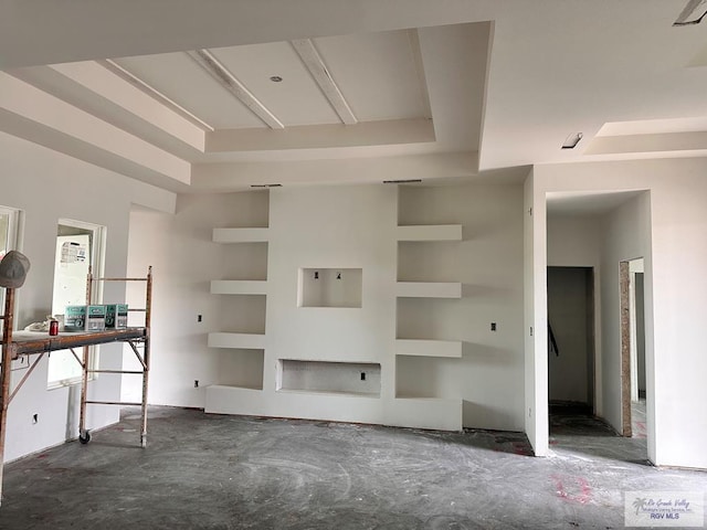 unfurnished living room featuring a raised ceiling and built in shelves