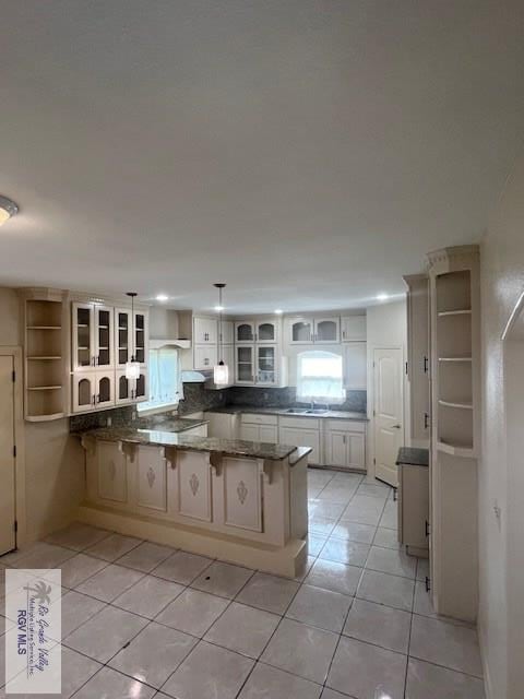 kitchen featuring tasteful backsplash, light tile patterned floors, decorative light fixtures, and kitchen peninsula