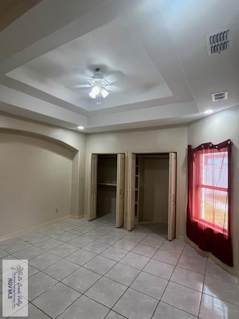 unfurnished bedroom featuring multiple closets, ceiling fan, a raised ceiling, and light tile patterned floors