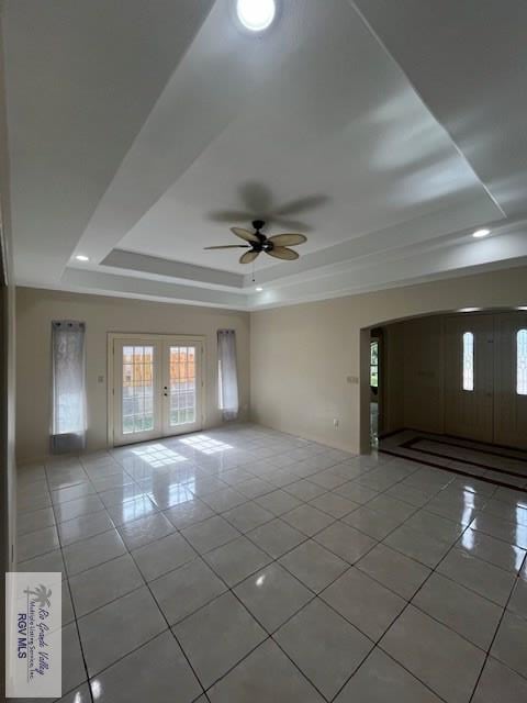 interior space featuring a raised ceiling, light tile patterned flooring, ceiling fan, and french doors