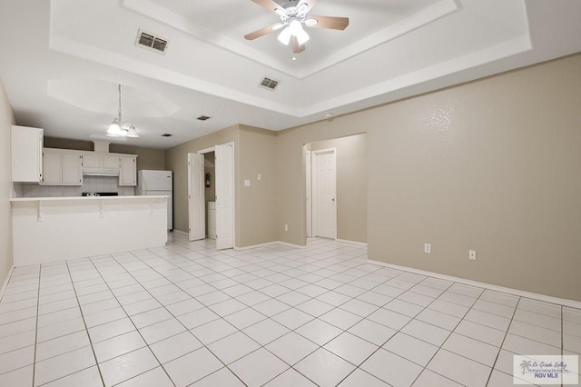 unfurnished living room featuring a raised ceiling, ceiling fan, and light tile patterned floors