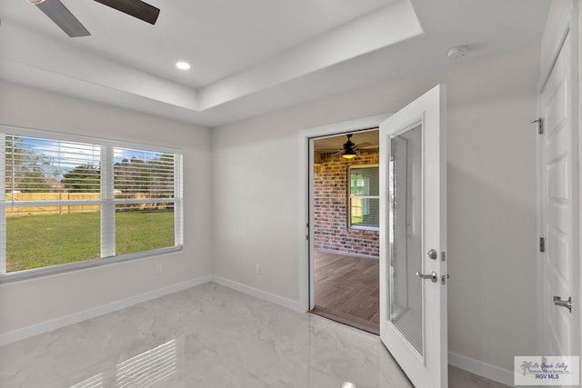 empty room with ceiling fan and a raised ceiling