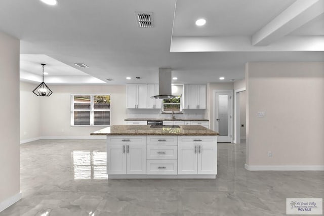 kitchen with white cabinetry, decorative light fixtures, dark stone countertops, a raised ceiling, and island exhaust hood