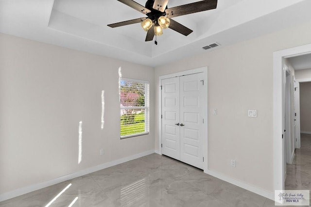 unfurnished bedroom with ceiling fan, a tray ceiling, and a closet