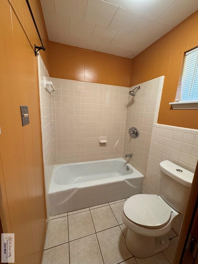 bathroom with tile patterned flooring, toilet, tile walls, and tiled shower / bath