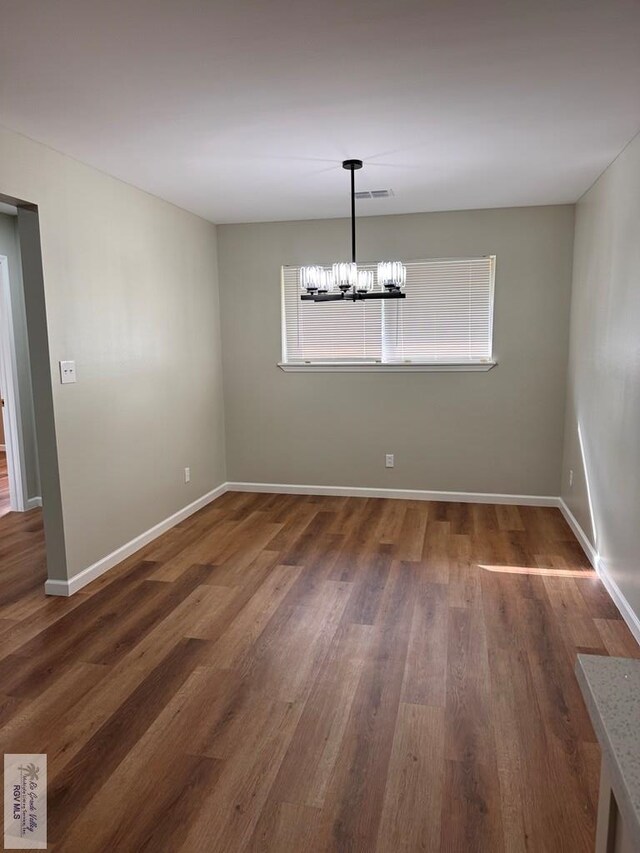 unfurnished dining area featuring dark wood-type flooring and a chandelier