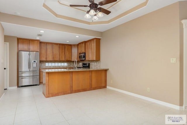 kitchen featuring tasteful backsplash, a tray ceiling, kitchen peninsula, ceiling fan, and stainless steel appliances