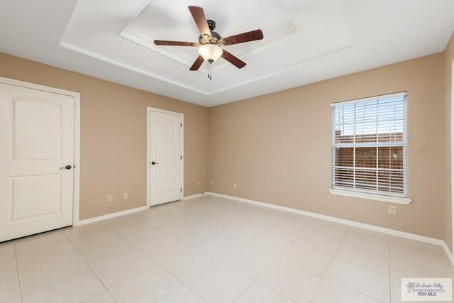 unfurnished bedroom with light tile patterned floors, a tray ceiling, and ceiling fan