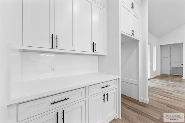 interior space featuring white cabinets, lofted ceiling, and light hardwood / wood-style flooring