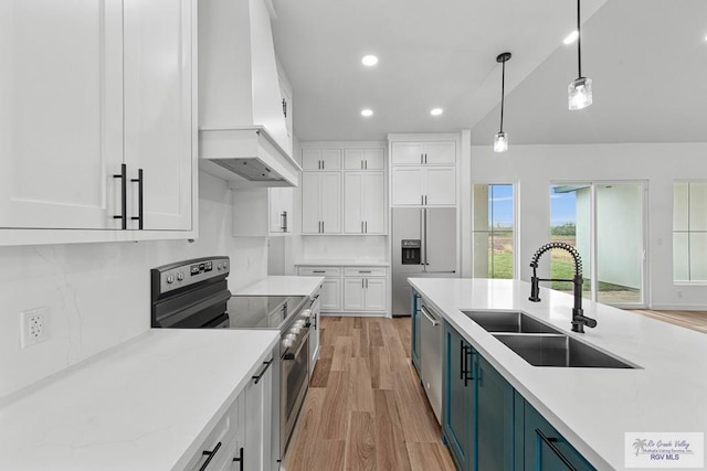 kitchen featuring appliances with stainless steel finishes, premium range hood, sink, white cabinets, and hanging light fixtures