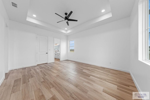 unfurnished bedroom with ceiling fan, a raised ceiling, and light wood-type flooring