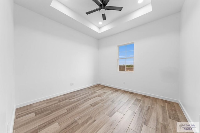 spare room featuring a raised ceiling, ceiling fan, and light wood-type flooring