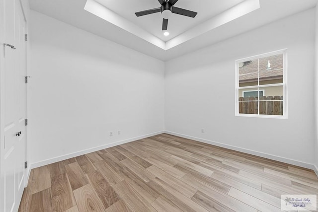 spare room with light hardwood / wood-style flooring, a raised ceiling, and ceiling fan